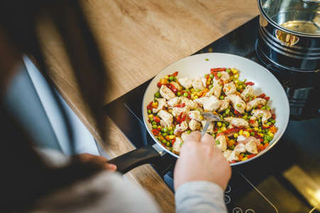 Top view on cooking pan with chicken meat and vegetables - unknown woman making healthy meal at kitchen at homeの写真素材