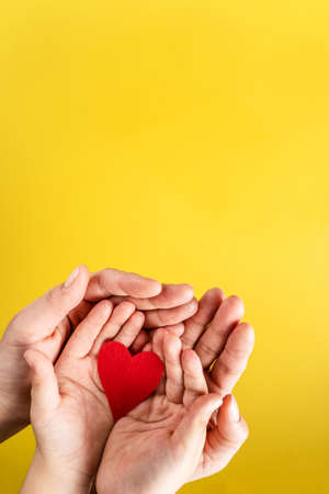 Red hart on palms of mother and son - Caucasian woman and child holding red hart shape above the modern abstract yellow background with copy space - Love care protection motherhood and family conceptの写真素材