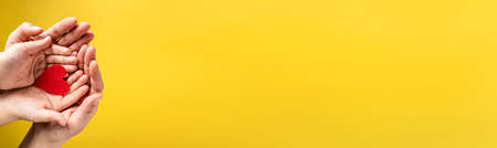 Red hart on palms of mother and son - Caucasian woman and child holding red hart shape above the modern abstract yellow background with copy space - Love care protection motherhood and family conceptの写真素材