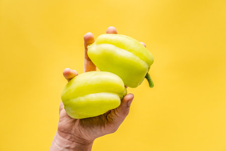 Hand of unknown person hold Fresh organic paprika bell peppers over the yellow background with copy space - modern healthy eating vegetarian or vegan food conceptの写真素材