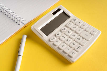 Office notebook with a pencil and a calculator on a yellow backgroundの写真素材