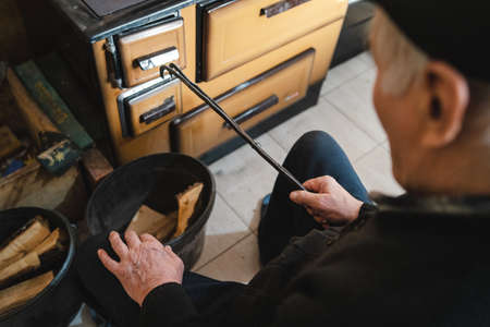 A senior man elderly caucasian grandfather farmer sitting by the stove kitchenの写真素材