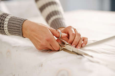 Close up on hands of unknown caucasian woman holding scissors cutting textile on the table at home...