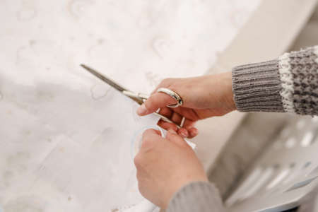 Close up on hands of unknown caucasian woman holding scissors cutting textile on the table at home...