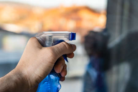 Close up on hand of unknown man using spray detergent to clean windowsの写真素材