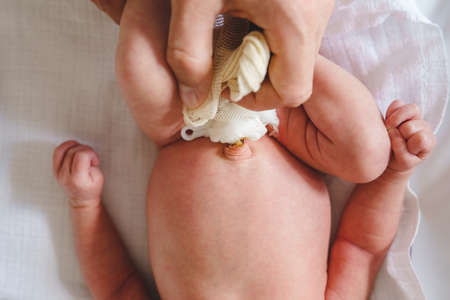 Hands of unknown man father caring for umbilical cord with clamp and bandage of newborn baby neonatal care parent clean navel of baby on bed at homeの写真素材