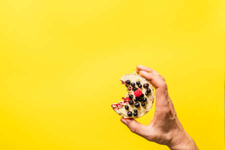 Hand holding crispy puffed rice cake with fresh fruit blueberries raspberries in front of the the yellow background - healthy organic vegetarian or vegan breakfast gluten free copy spaceの写真素材