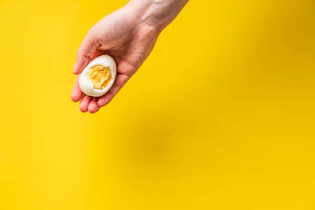 Close up on hand holding boiled egg with yolk in front of yellow backgroundの写真素材