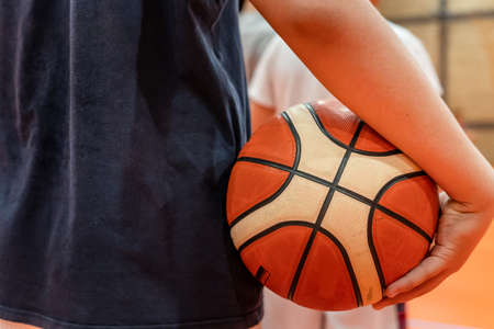 Close up on basketball ball in hands of unknown caucasian boy child teenager holding it on the training or waiting for the game to play sport development and growing up conceptの写真素材