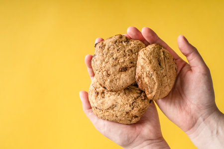 Close up on hands of unknown caucasian woman holding homemade baked fresh crunchy chip cookie...