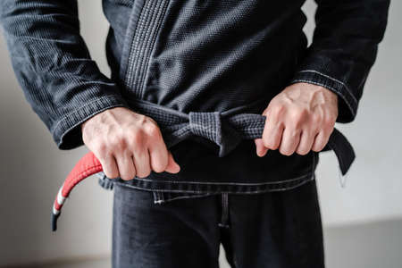 Front view of hands of unknown caucasian man in kimono gi standing while holding and tie knot black bjj belt brazilian jiu jitsu concept copy spaceの写真素材