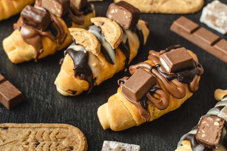 Close up on homemade baked sweet croissants on the black plate with chocolate biscuit and cream on the tableの写真素材