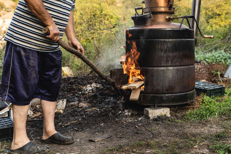 Unknown man putting woods on fire on cooking Homemade illegal distillery on the farm making domestic brandy vodka Rakija whiskey the traditional way of making strong drinks in balkan Serbiaの写真素材