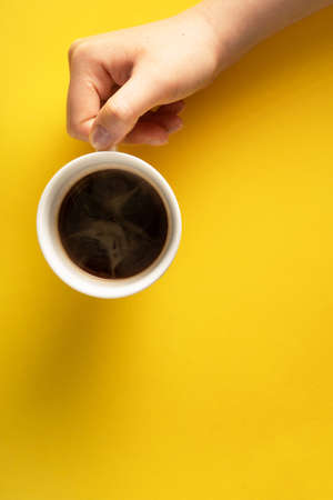 Flat lay of female woman hand holding cup of espresso coffee with copy space on yellow backgroundの写真素材