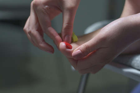 Side view on hand applying gel lac on feet toes nails - Unknown woman doing pedicure on her feet at home - Nail polish painting on foot fingernails - Top view selective focus dark room beauty conceptの写真素材