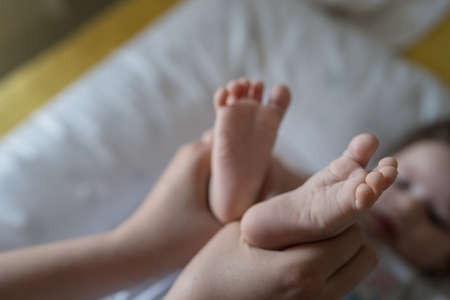 unknown caucasian mother holding feet of her baby lying on the bed motherhood and parenting concept copy spaceの写真素材