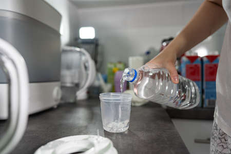 Hand of unknown woman pouring distillate water to plastic cup on the kitchen counter preparingの写真素材