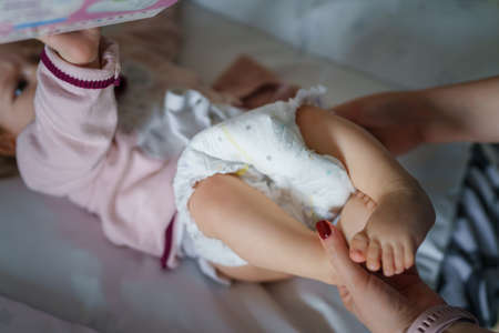 Close up hands of unknown caucasian woman mother changing diapers to her six months old baby girl daughter while lying on the bed at home - parenthood and motherhood care conceptの写真素材