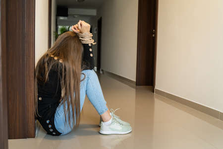 One unknown woman with tied hands with rope sitting on the floor in corridor desperate female victim human trafficking and modern slavery conceptの写真素材