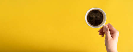 Flat lay of female woman hand holding cup of espresso coffee with copy space on yellow backgroundの写真素材