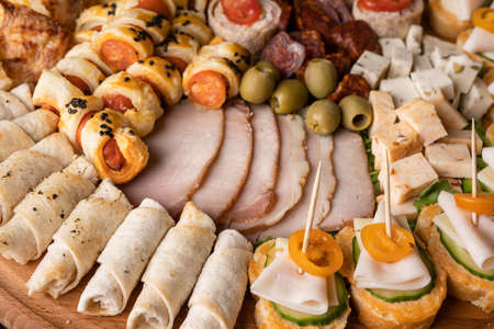 Close up on cheese and ham rolls on the wooden board plate with various food ready to eat - appetizer on the table full frameの写真素材