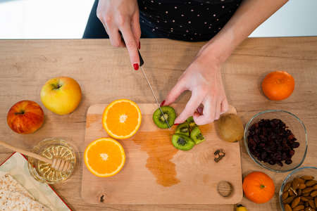Close up on hand of unknown caucasian woman holding knife cutting kiwi and oranges top view copy...