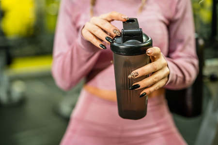 Front view on hands of unknown caucasian woman female athlete holding plastic bottle supplement shaker while training at gym real people copy spaceの写真素材