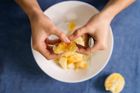 Close up on hands of unknown caucasian woman separating orange slices over the bowl on the table at...