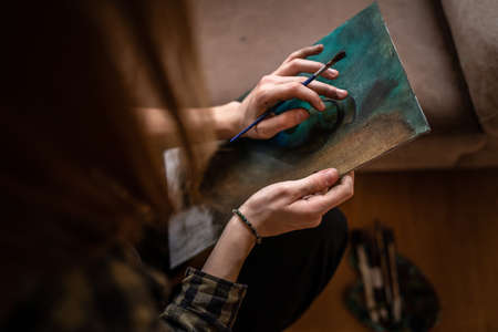 Close up on hands of unknown female artist caucasian woman or girl painting on canvas using brush...