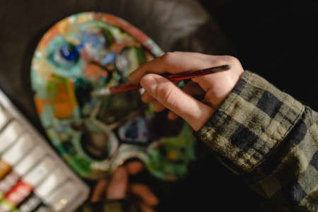 Close up on hands of unknown female artist painter holding color palette and paintbrush brushes ready to make art leisure activity professional or amateur artist painting concept top view copy spaceの写真素材