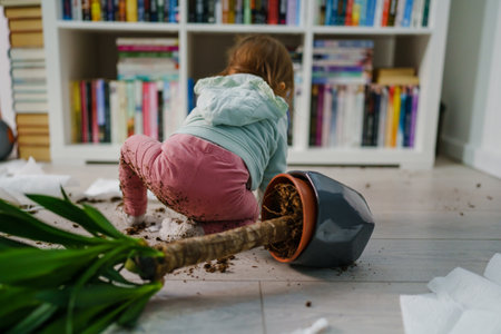 one caucasian baby girl making mess playing and mischief with bad behavior ripping paper towel and flower pot cruched on the floor naughty kid at home childhood and growing up misbehavior conceptの写真素材