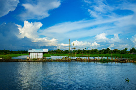 A small old shack at the center of the backwater under a white and blue cloudy sky, Kerala backwaters photography during day time Kadamakkudy Kerala, Stripe of coconut trees between a cloudy sky and river.のeditorial素材