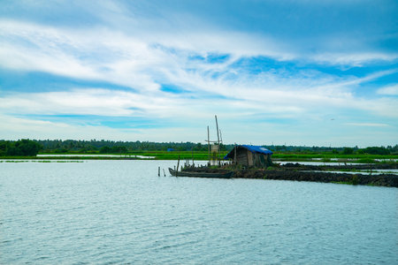 A small wooden fishing boat lying near an old hut, Kerala backwaters landscape photography, Kerala backwaters photography during day time Kadamakkudy Keralaのeditorial素材