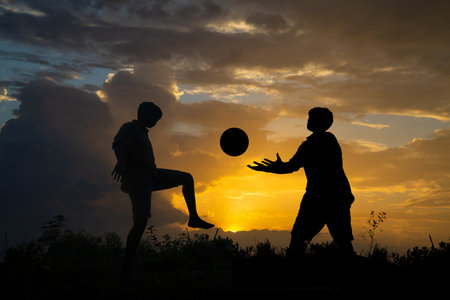 Silhouette of boy playing football during sky sunset background, Silhouette Boy Standing On Field Against blue cloudy Skyの写真素材