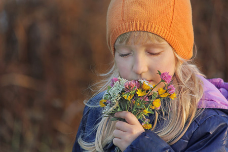 Beautiful blond girl closing her eyes sniffs the bouquet of wildflowers. Autumn.の写真素材