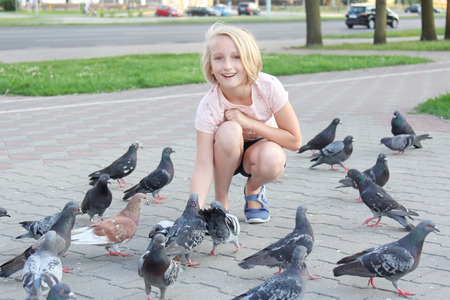 Cheerful girl feeds pigeons on the street in the cityの写真素材