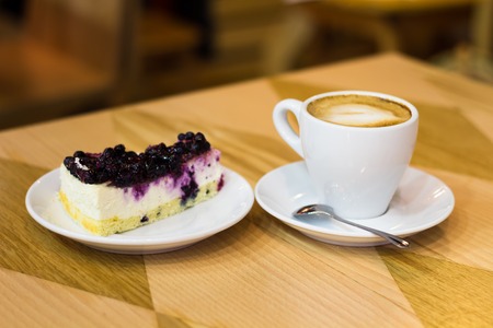 Cheesecake with currant and white cup of coffee on the wooden tableの写真素材