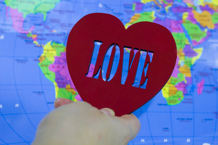 Big red heart with the inscription love on a background map of the earth in handの写真素材