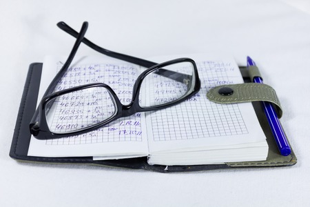Glasses notebook and pen on a table on a white backgroundの写真素材