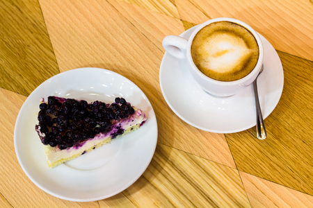 Cheesecake with currant and white cup of coffee on the wooden tableの写真素材