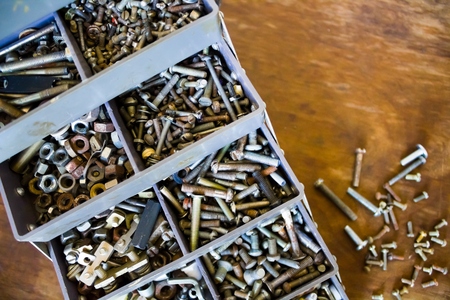 A lot of small details screws bolts nuts in a special box for tools on a wooden backgroundの写真素材