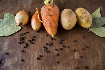 Vegetables on the table carrot onion potato near spices of black pepper and bay leaf on the wooden...