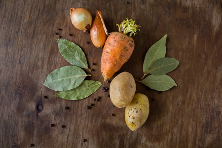Vegetables on the table carrot onion potato near spices of black pepper and bay leaf on the wooden...