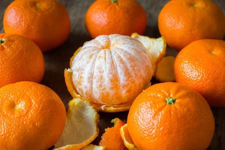 Delicious fresh tangerines and a big mandarin without peel  lie on a wooden tableの写真素材