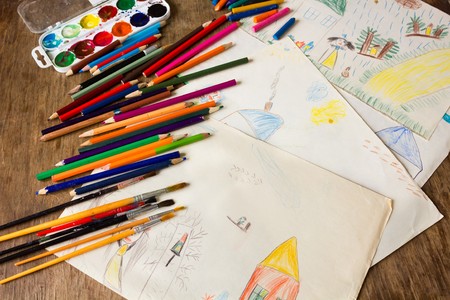 Many colored pencils paint brush lying on a background of children's drawings