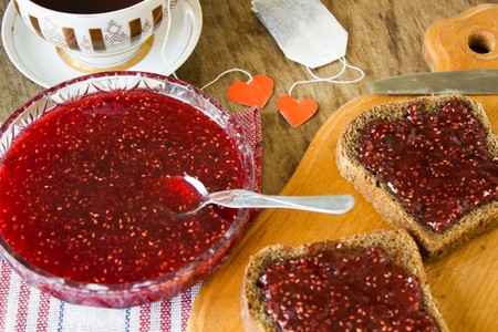 A light breakfast or lunch a lot of raspberry jam in a plate and a slice of black bread with jam on...