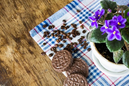 Gentle purple violets on a blue checkered napkin coffee beans and chocolate cookies close up viewの写真素材