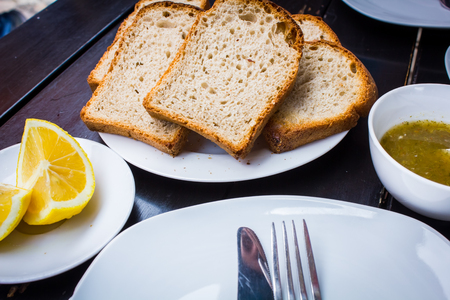 Delicious fresh sliced bread on a plate next to the chopped lemon and tableware on a stylish black...
