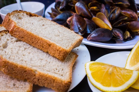 Delicious mussels fresh tomato salad sauce sliced bread and cut lemon on a stylish black tableの写真素材