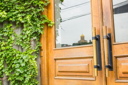 Beautiful stylish wooden door next to ivy and a reflection of the Cathedral of Tbilisi, Georgiaの写真素材